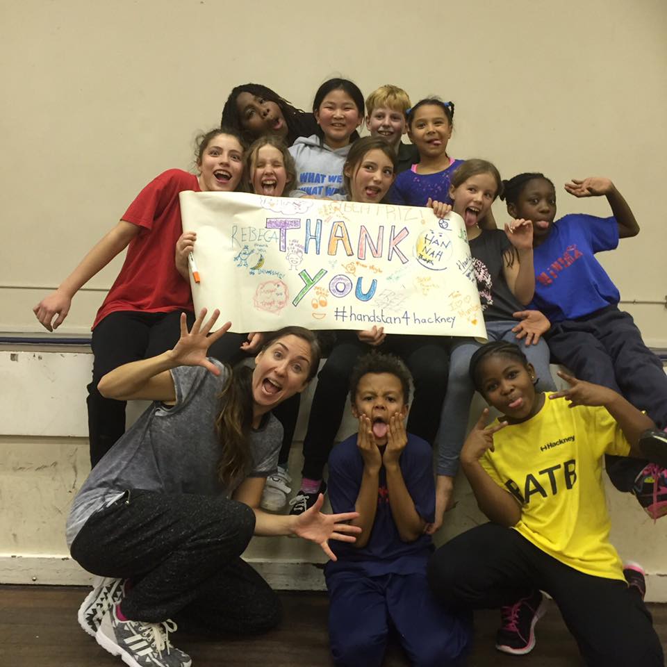 A group of smiling children hold a homemade banner reading, thank you.