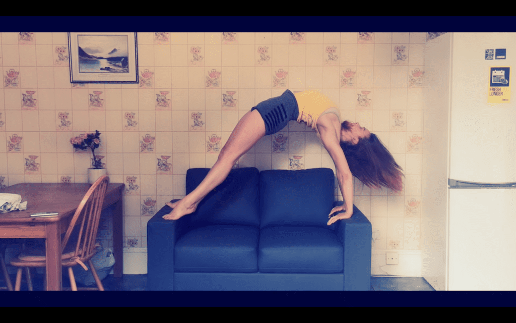 a woman in a high bridge on her blue sofa, the couch sits between a  kitchen table and a fridge