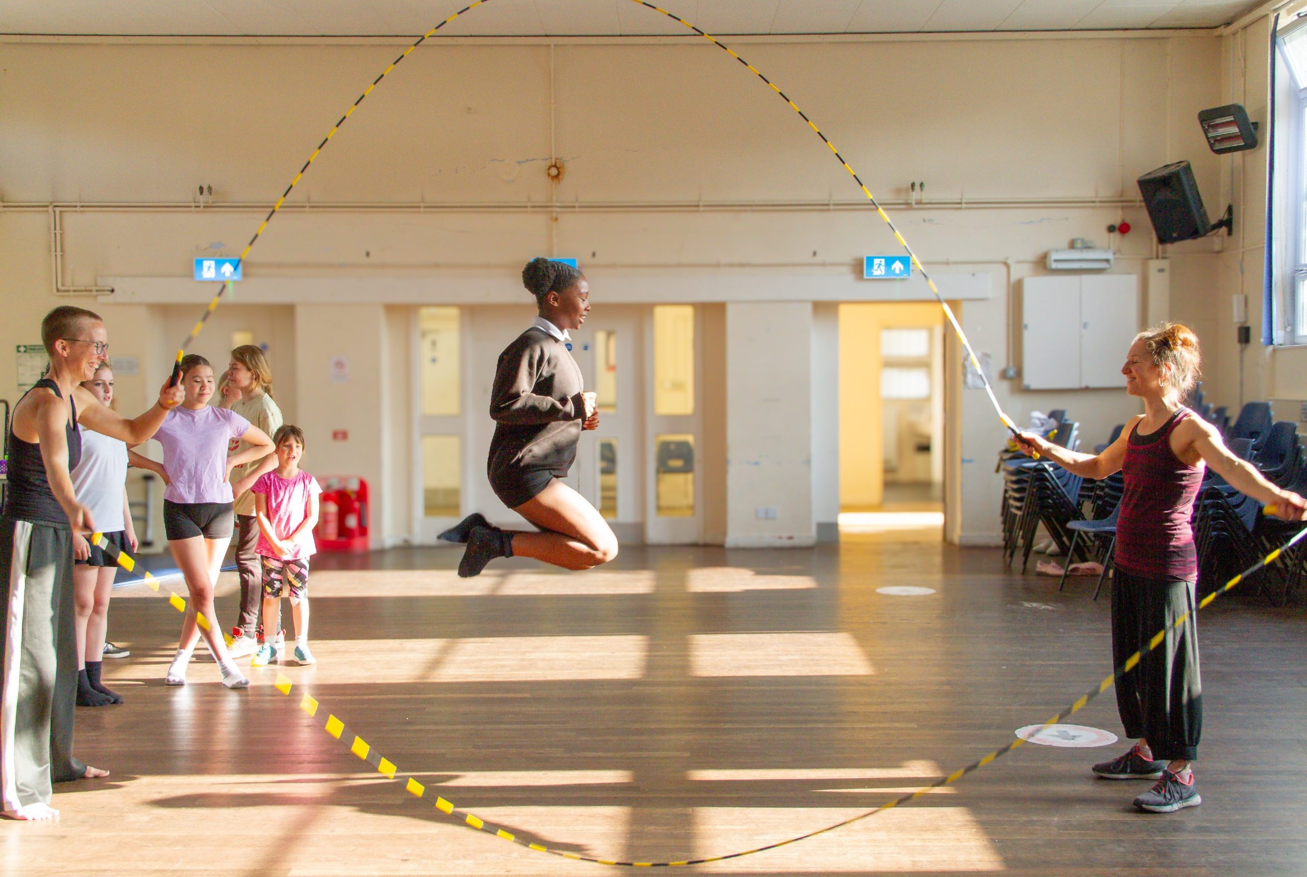 Some people double dutch skipping in a brightly lit hall.